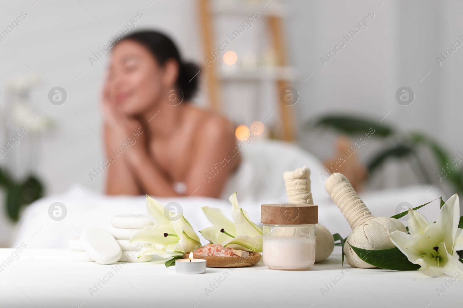 Beautiful woman relaxing on massage couch indoors, focus on different spa products and lily flowers Photo of Beautiful woman relaxing on massage couch indoors, focus on different spa products and lily flowers