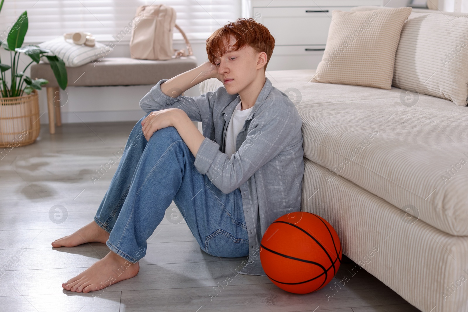 Teen problems. Depressed teenage boy with basketball ball on floor indoors Photo of Teen problems. Depressed teenage boy with basketball ball on floor indoors
