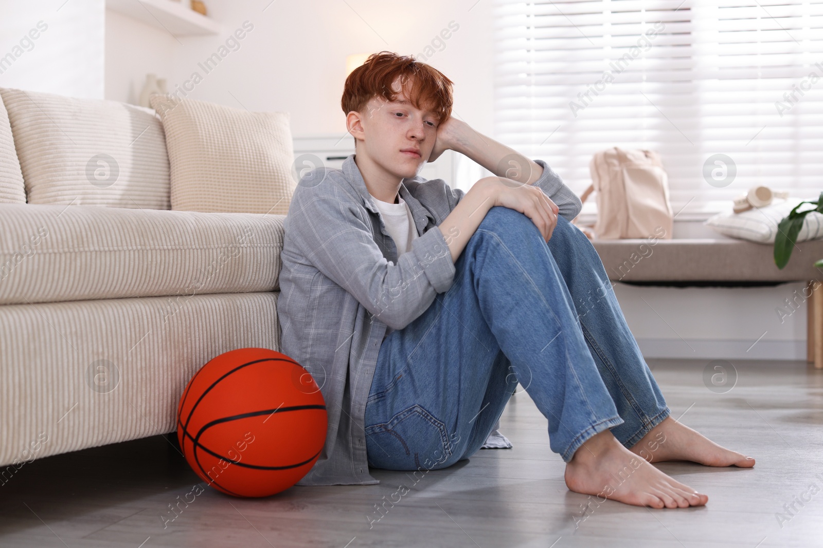 Teen problems. Depressed teenage boy with basketball ball on floor indoors Photo of Teen problems. Depressed teenage boy with basketball ball on floor indoors