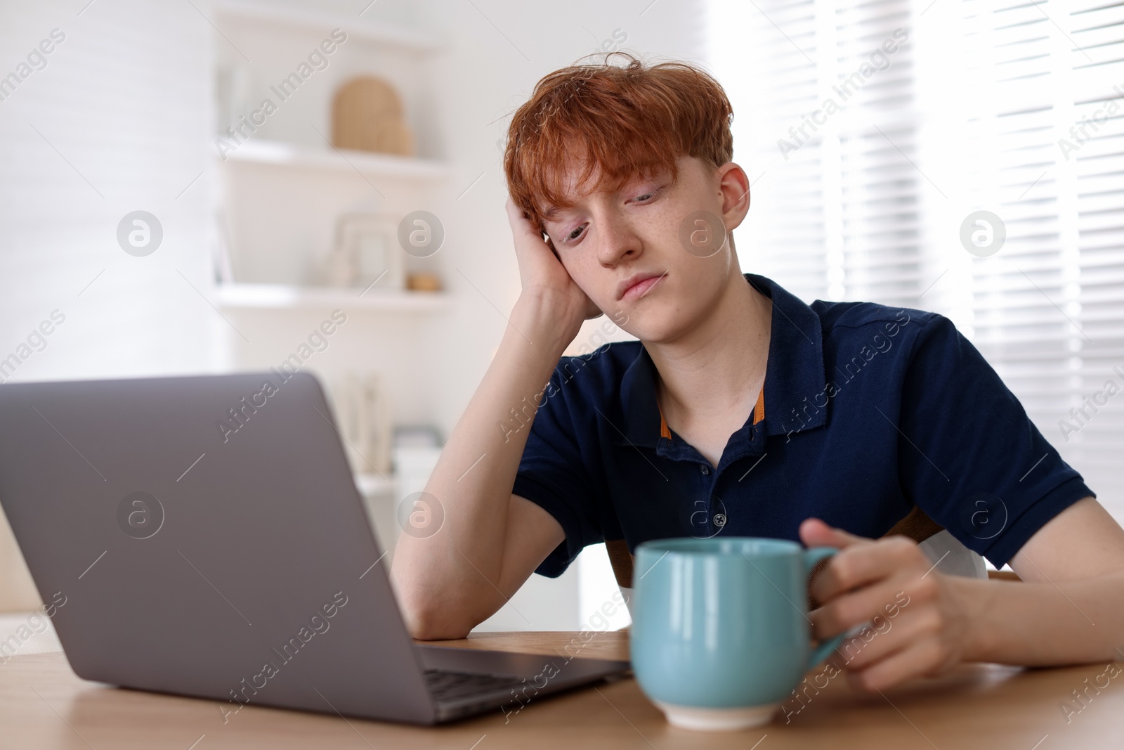 Teen problems. Depressed teenage boy with drink and laptop at desk indoors Photo of Teen problems. Depressed teenage boy with drink and laptop at desk indoors
