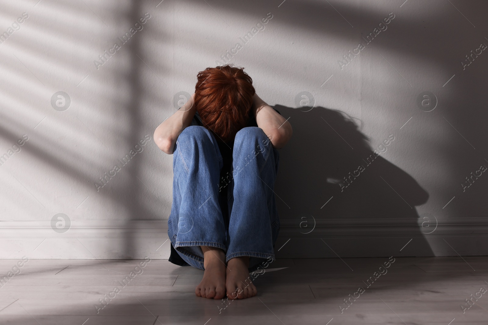 Teen problems. Depressed teenage boy on floor near grey wall Photo of Teen problems. Depressed teenage boy on floor near grey wall