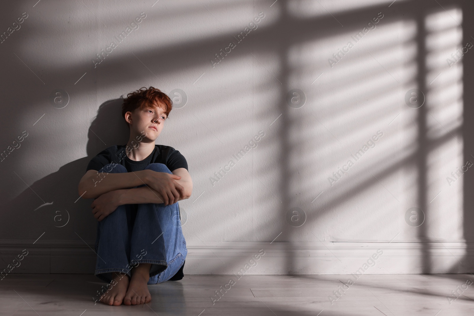 Teen problems. Depressed teenage boy on floor near grey wall, space for text Photo of Teen problems. Depressed teenage boy on floor near grey wall, space for text
