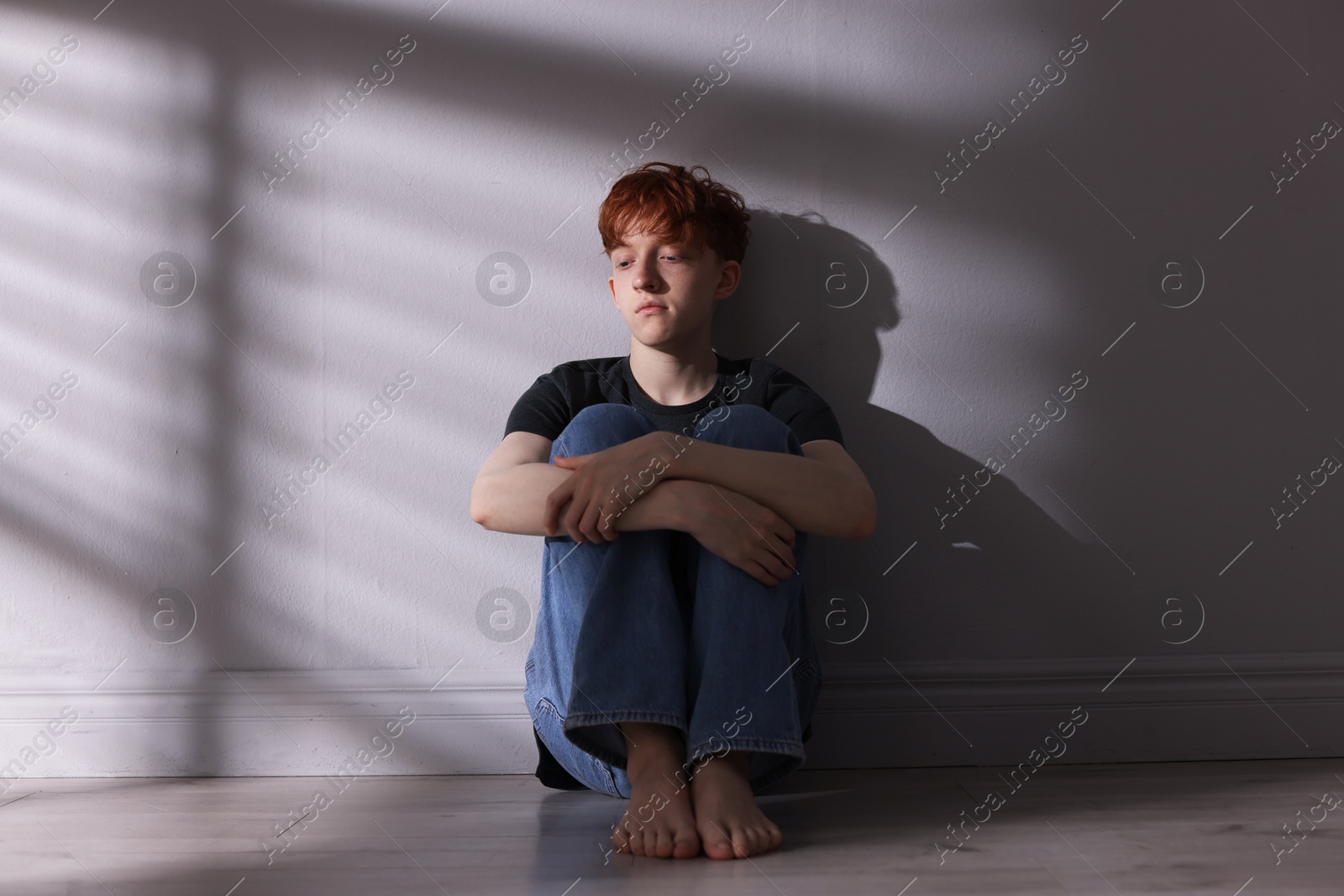 Teen problems. Depressed teenage boy on floor near grey wall Photo of Teen problems. Depressed teenage boy on floor near grey wall