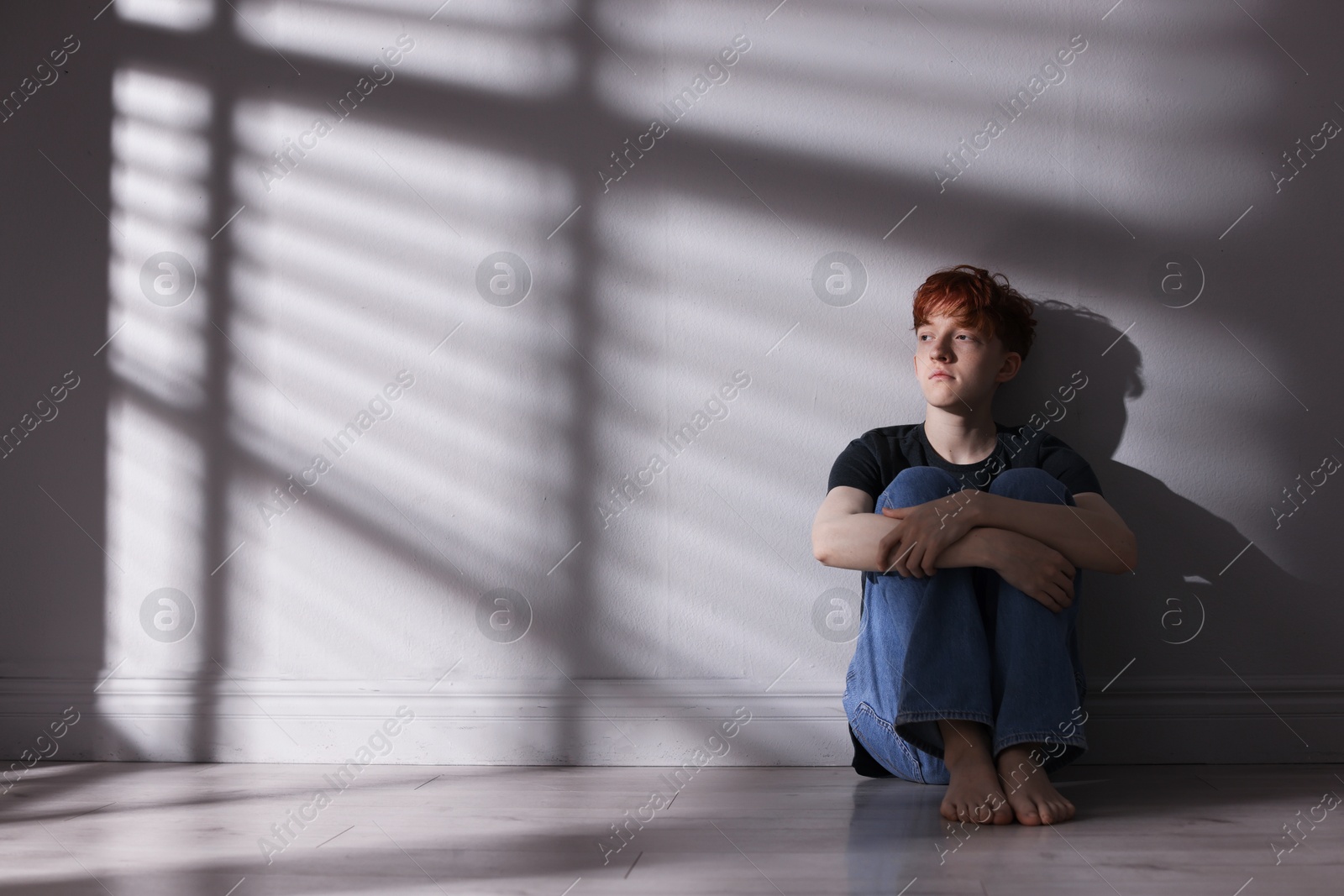 Teen problems. Depressed teenage boy on floor near grey wall, space for text Photo of Teen problems. Depressed teenage boy on floor near grey wall, space for text