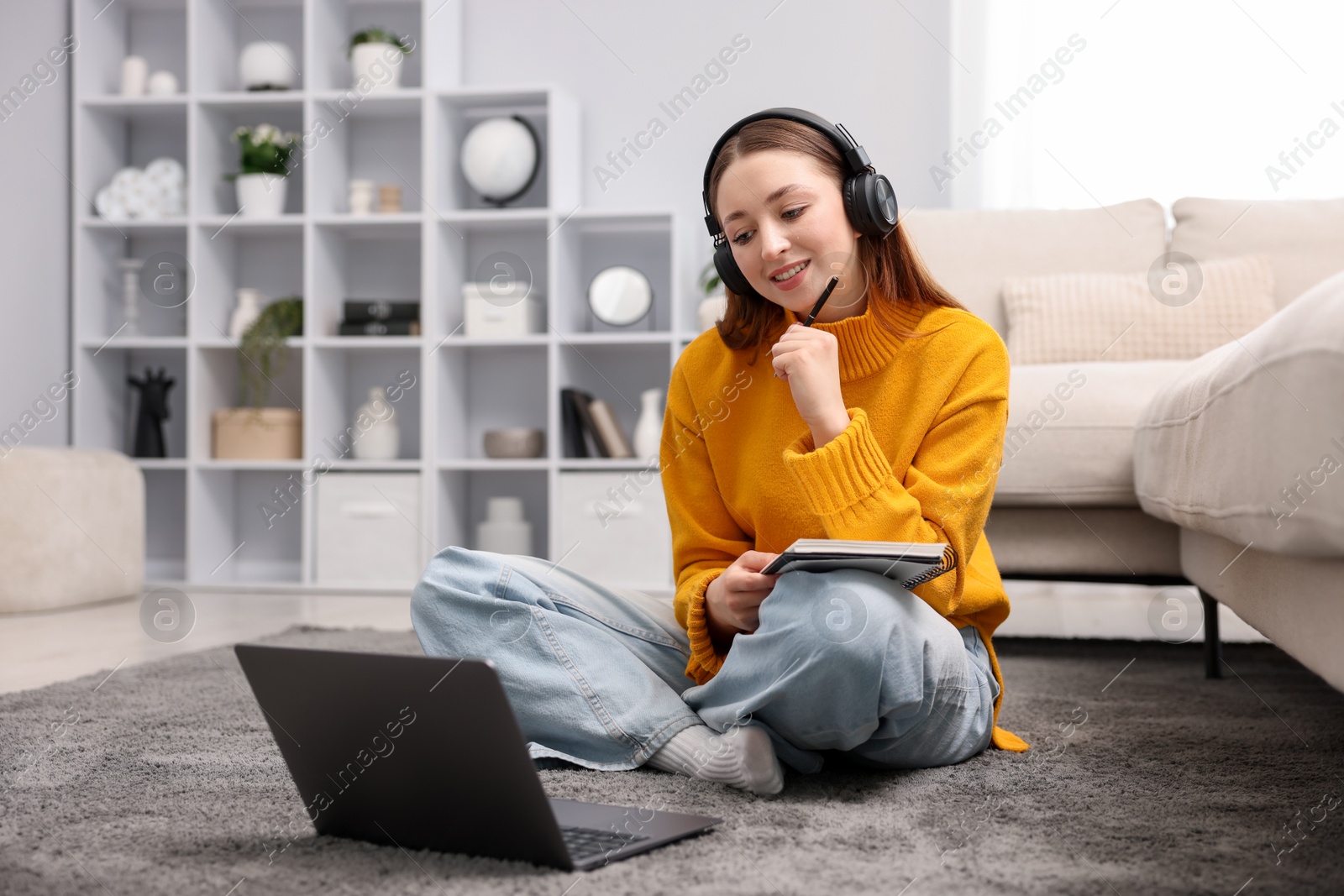 Teenage girl in headphones doing homework near laptop on floor at home Photo of Teenage girl in headphones doing homework near laptop on floor at home