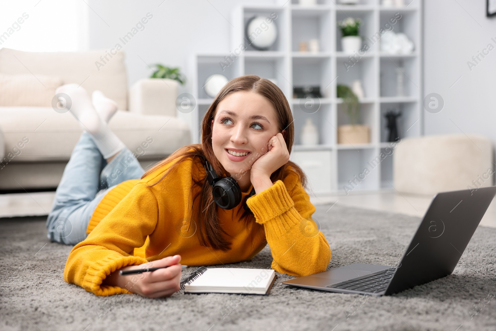 Photo of Teenage girl with headphones doing homework near laptop on floor at home