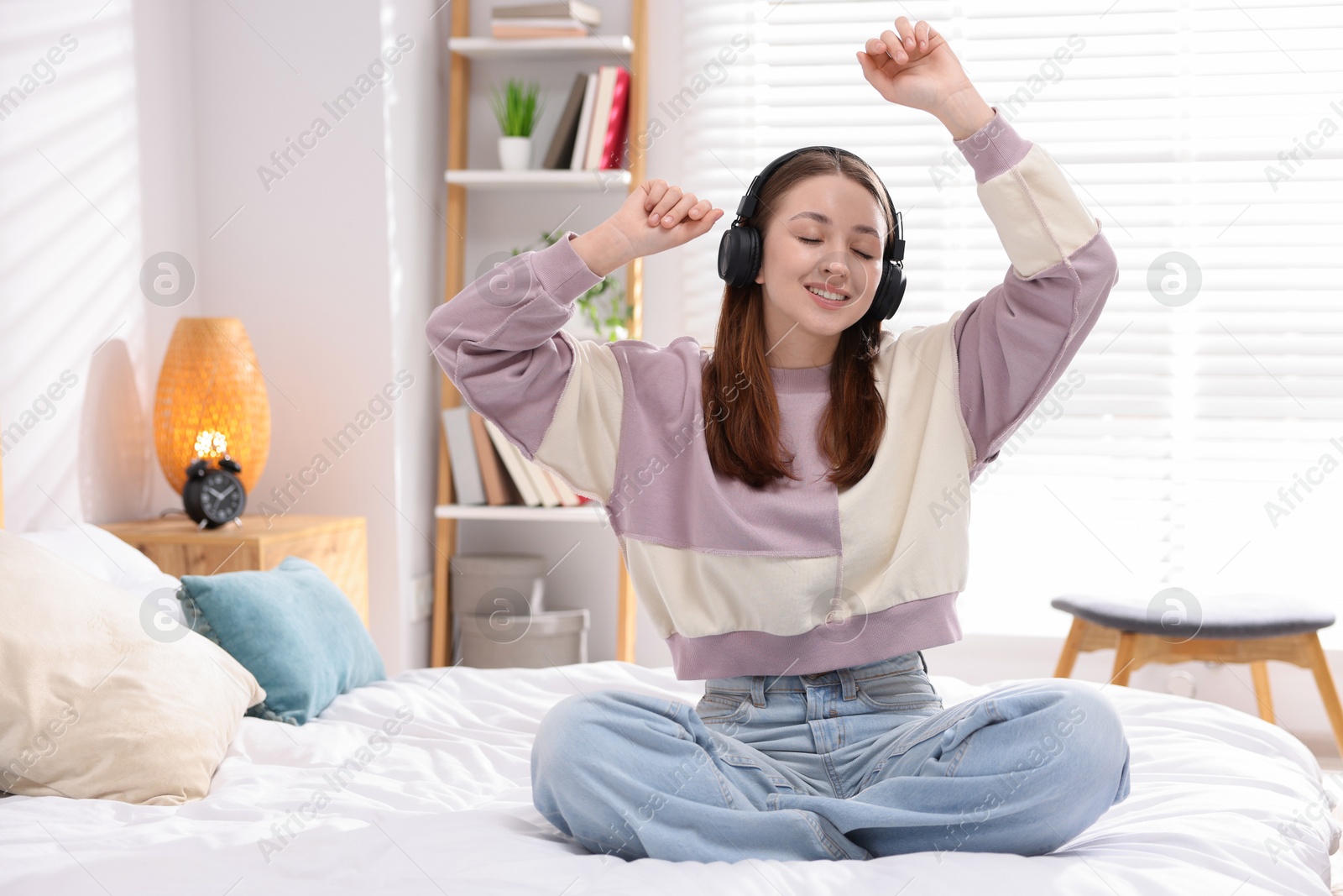 Photo of Teenage girl in headphones listening to music on bed at home