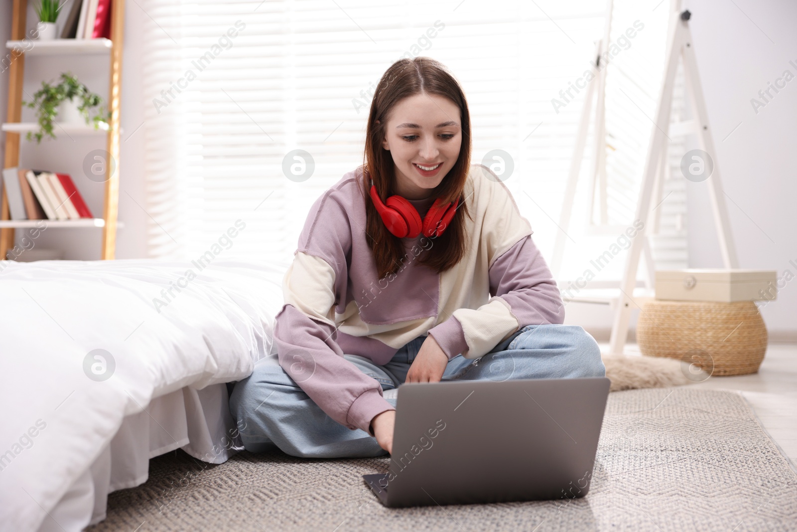 Teenage girl with headphones near laptop on floor at home Photo of Teenage girl with headphones near laptop on floor at home