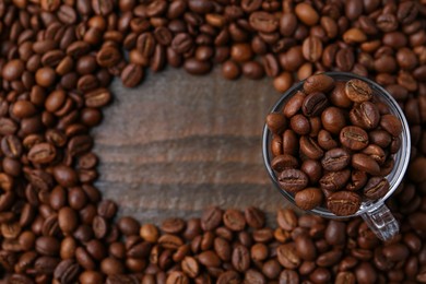 Photo of Aromatic coffee beans and glass cup on wooden table, flat lay. Space for text