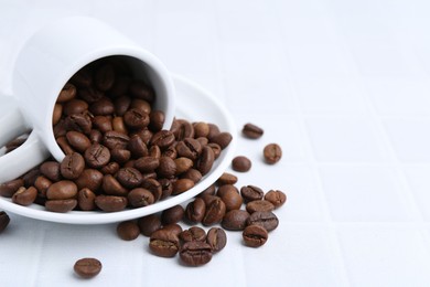Photo of Aromatic coffee beans, cup and saucer on white tiled table, closeup. Space for text