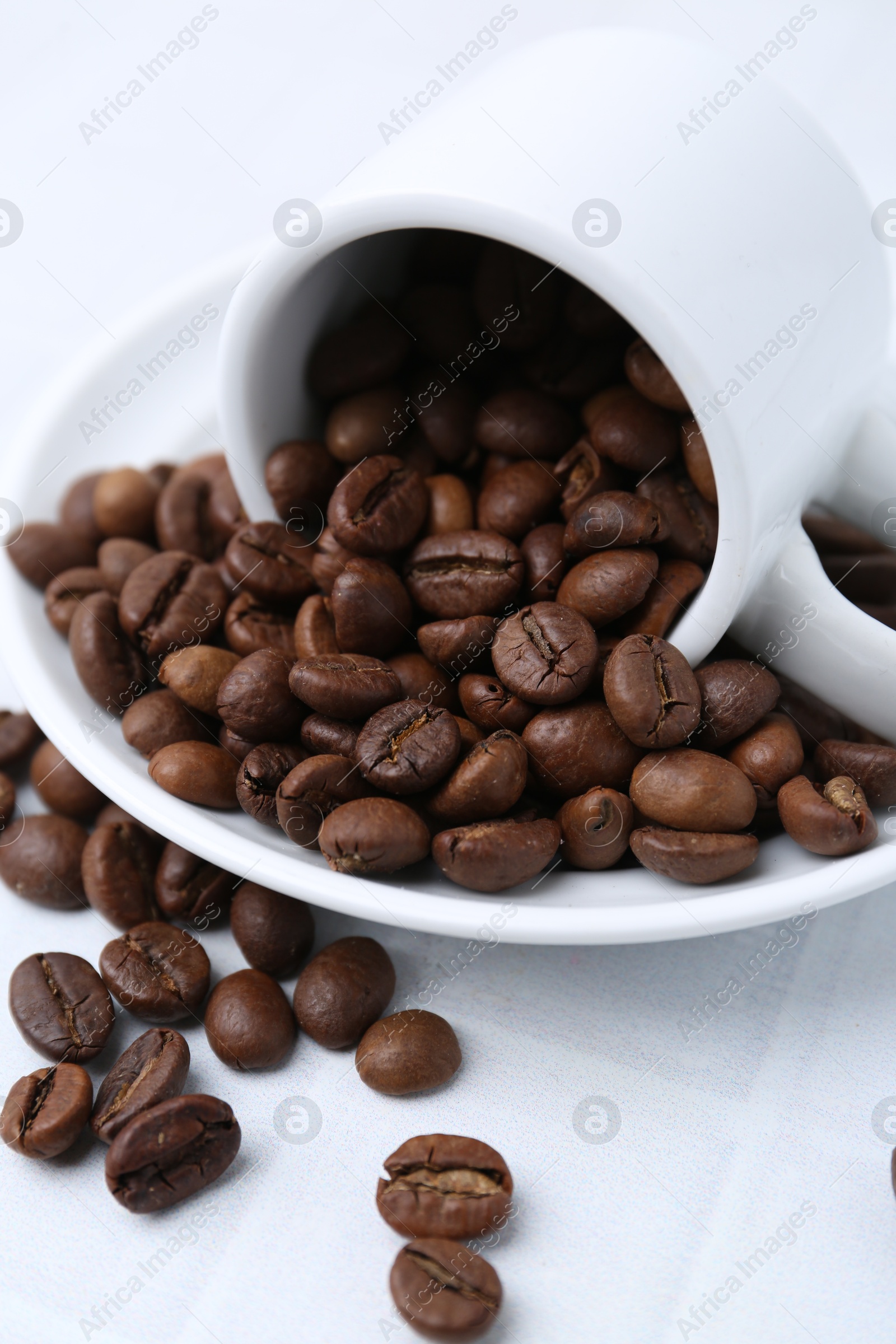 Aromatic coffee beans, cup and saucer on white table, closeup Photo of Aromatic coffee beans, cup and saucer on white table, closeup
