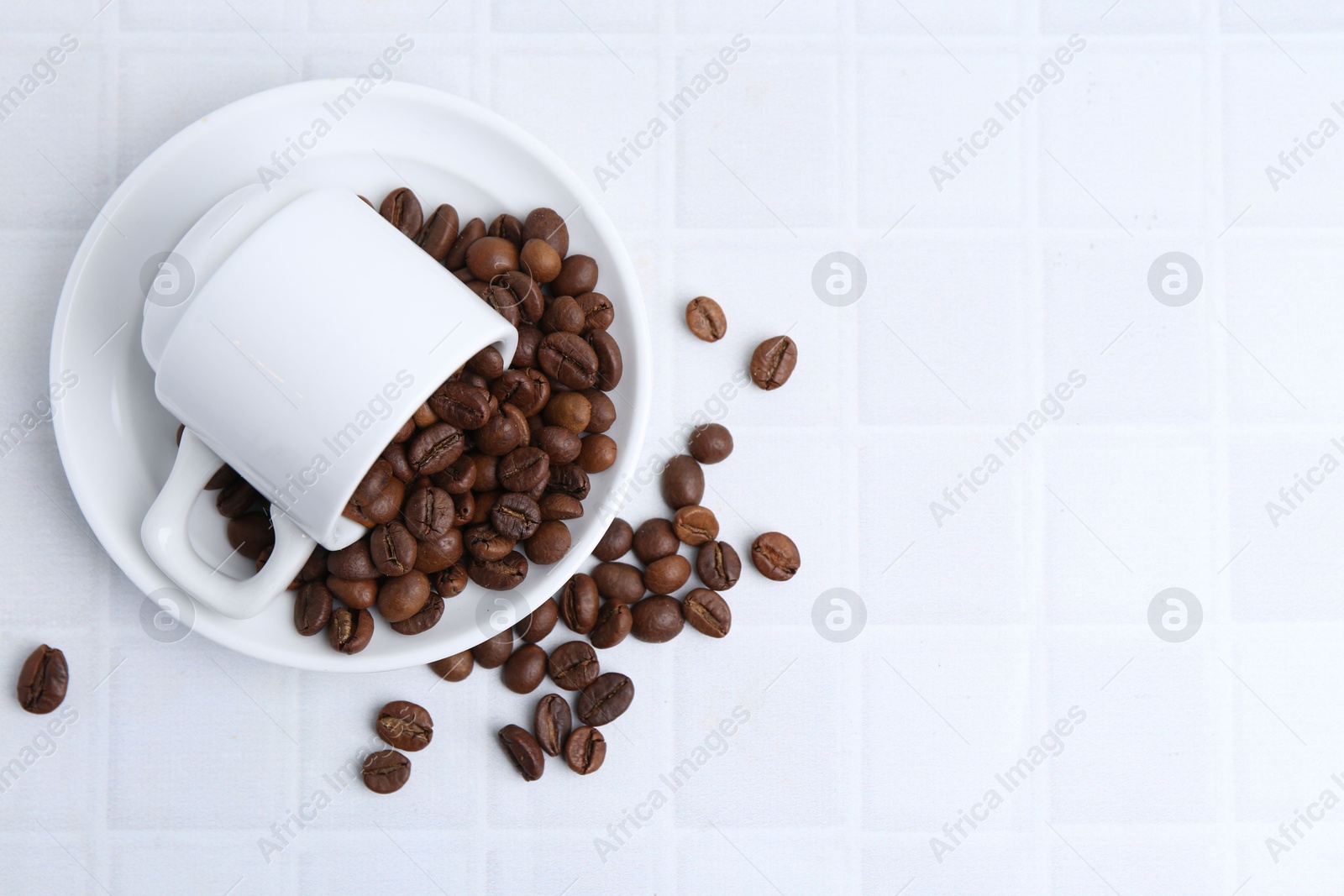 Aromatic coffee beans, cup and saucer on white tiled table, flat lay. Space for text Photo of Aromatic coffee beans, cup and saucer on white tiled table, flat lay. Space for text