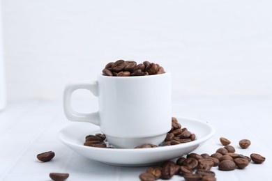 Photo of Aromatic coffee beans, cup and saucer on white table, closeup
