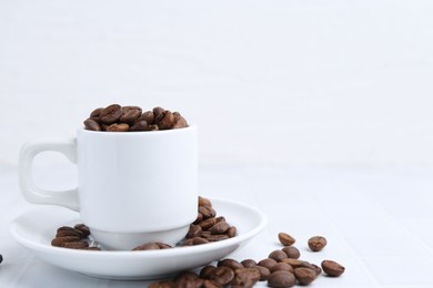 Photo of Aromatic coffee beans, cup and saucer on white table, closeup. Space for text