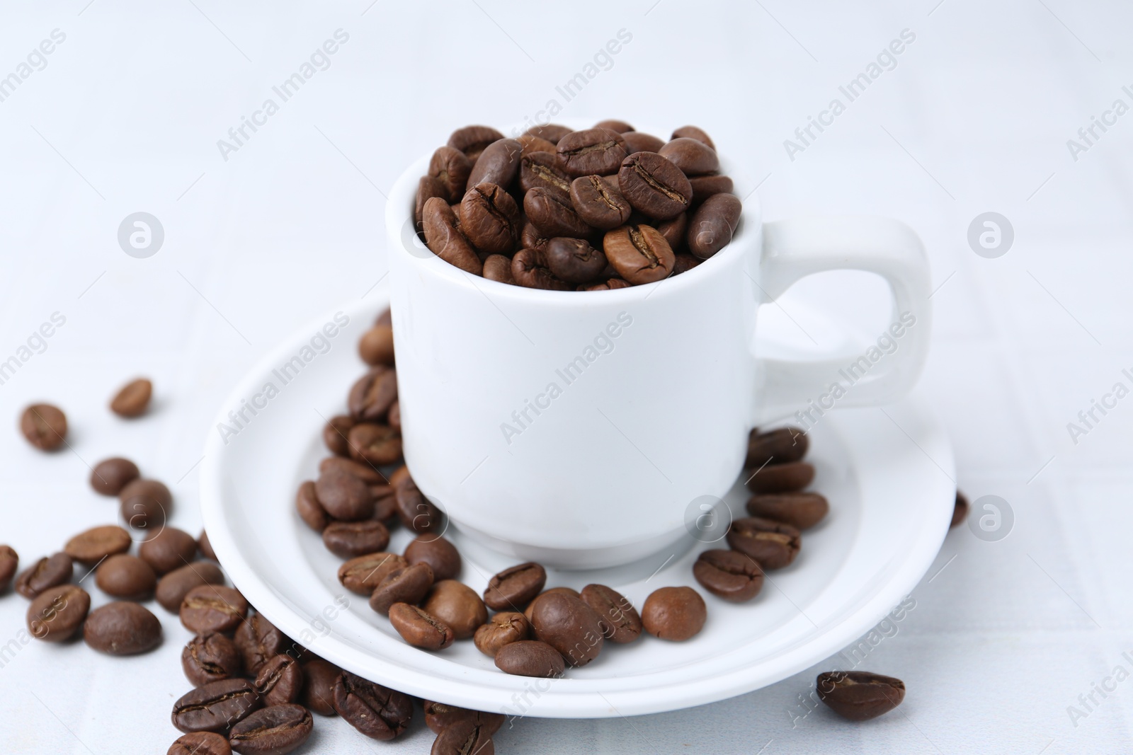 Aromatic coffee beans, cup and saucer on white table, closeup Photo of Aromatic coffee beans, cup and saucer on white table, closeup