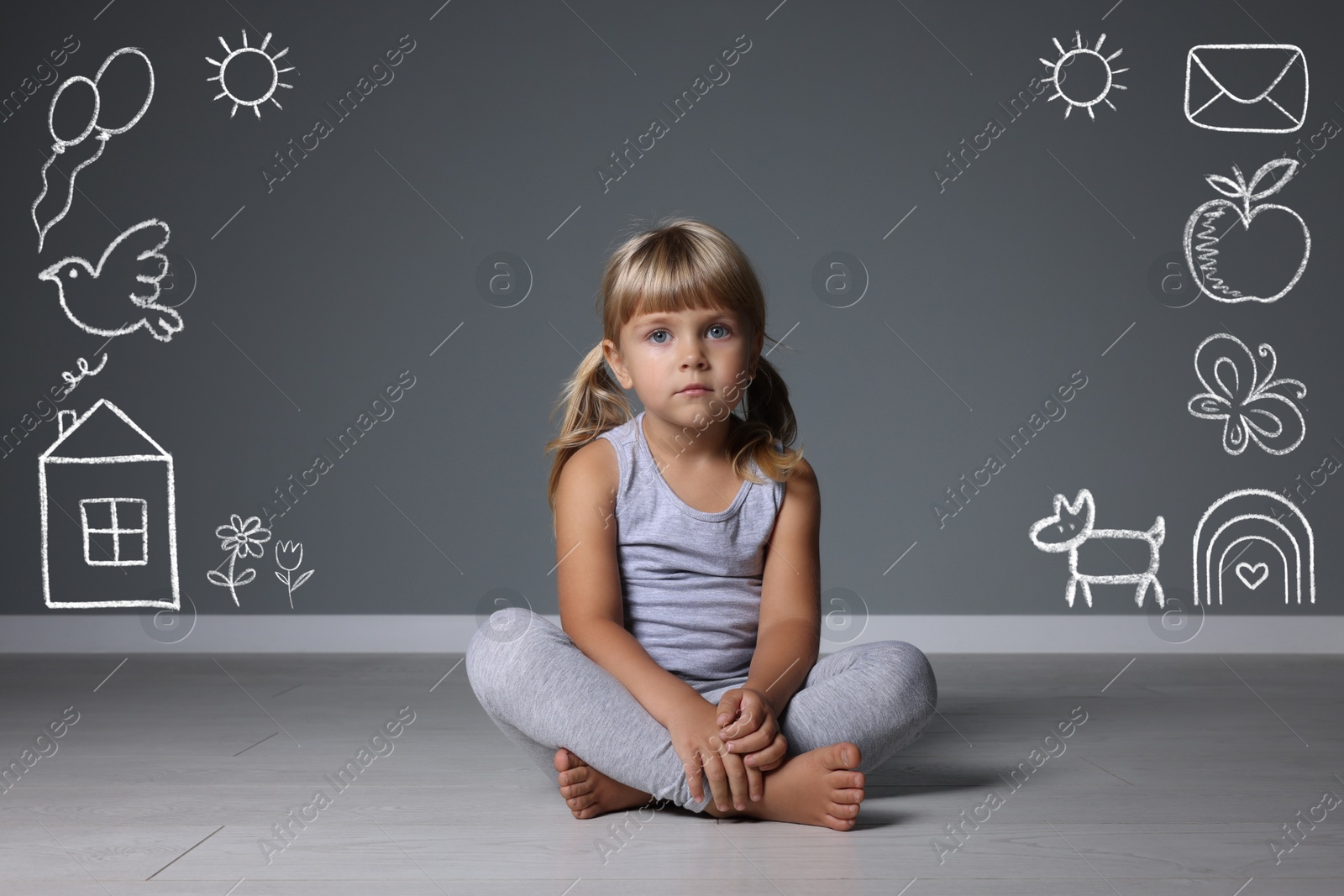 Image of Orphanage. Sad little girl on floor near grey wall with different drawings