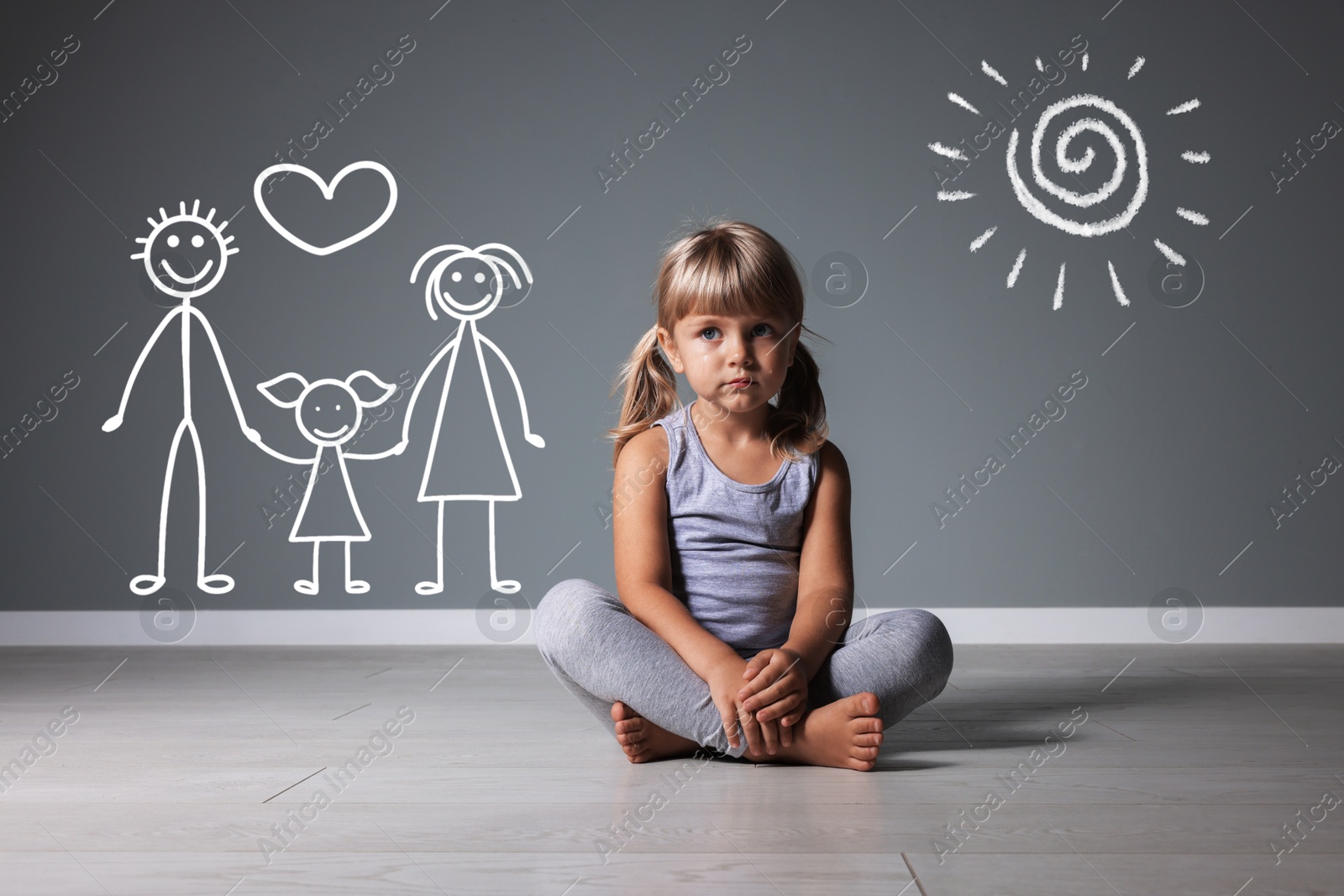 Image of Orphanage. Sad little girl on floor near grey wall with drawing of happy family and sun