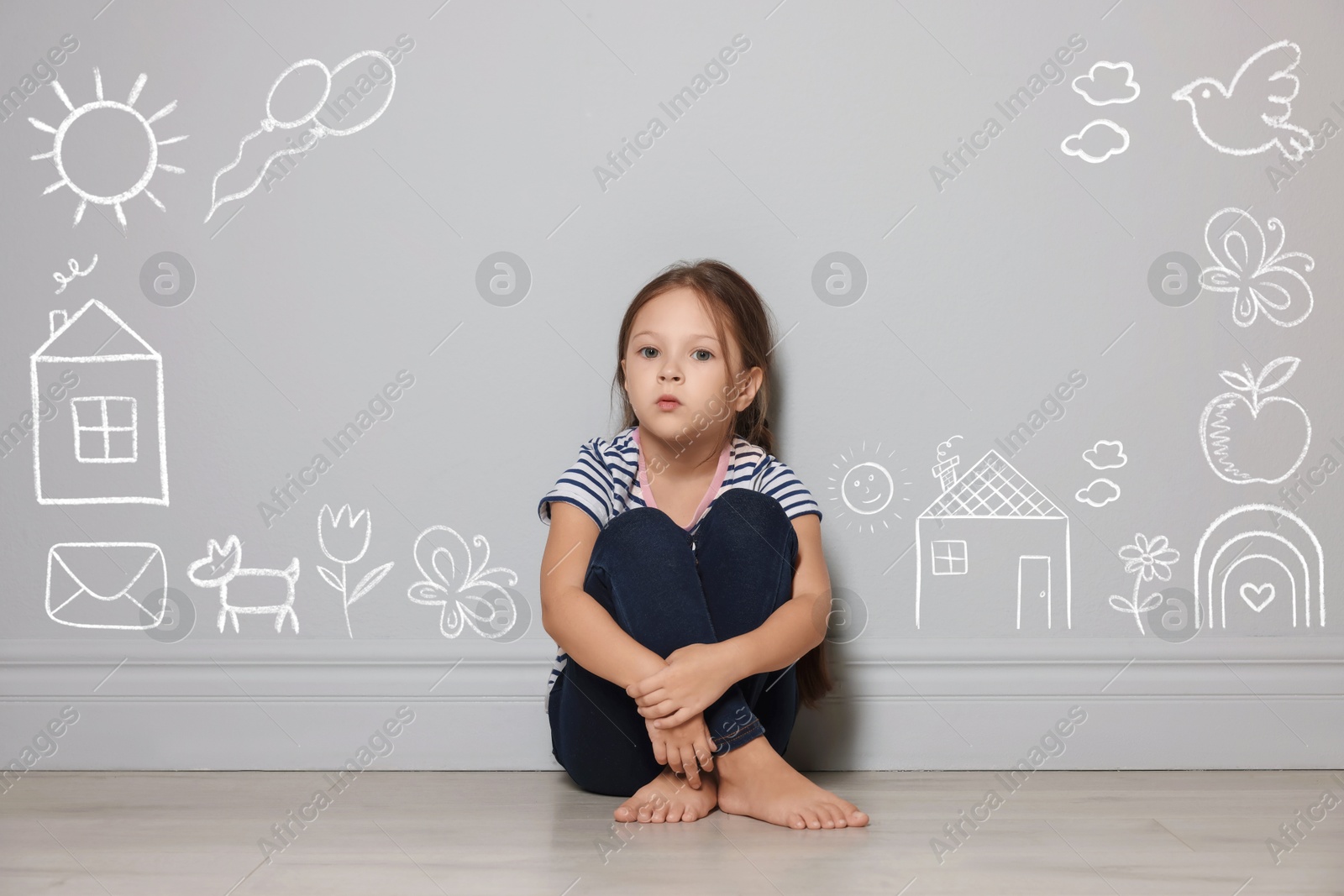 Image of Orphanage. Sad little girl on floor near grey wall with different drawings