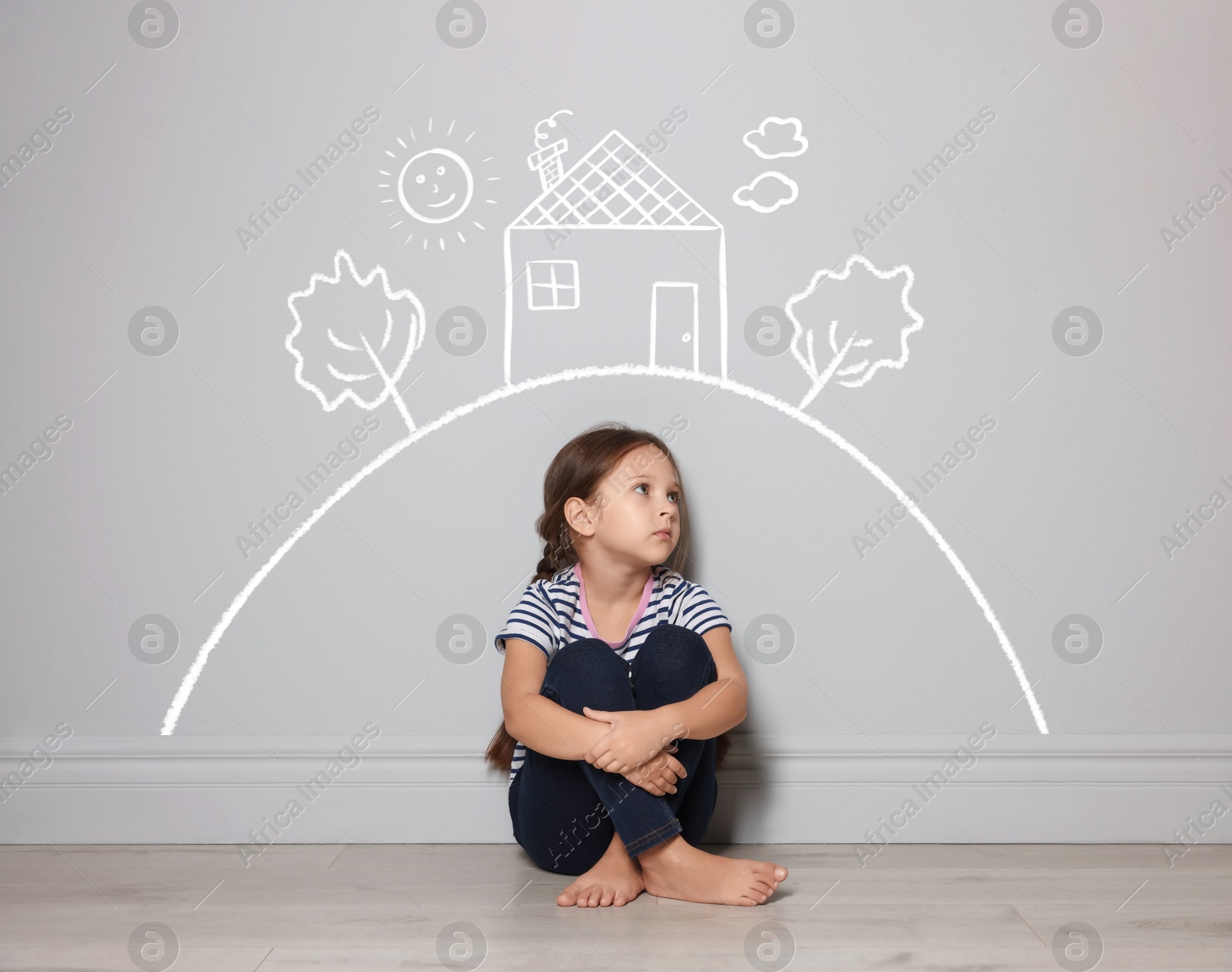 Image of Orphanage. Sad little girl on floor near grey wall with drawings of house, sun and trees