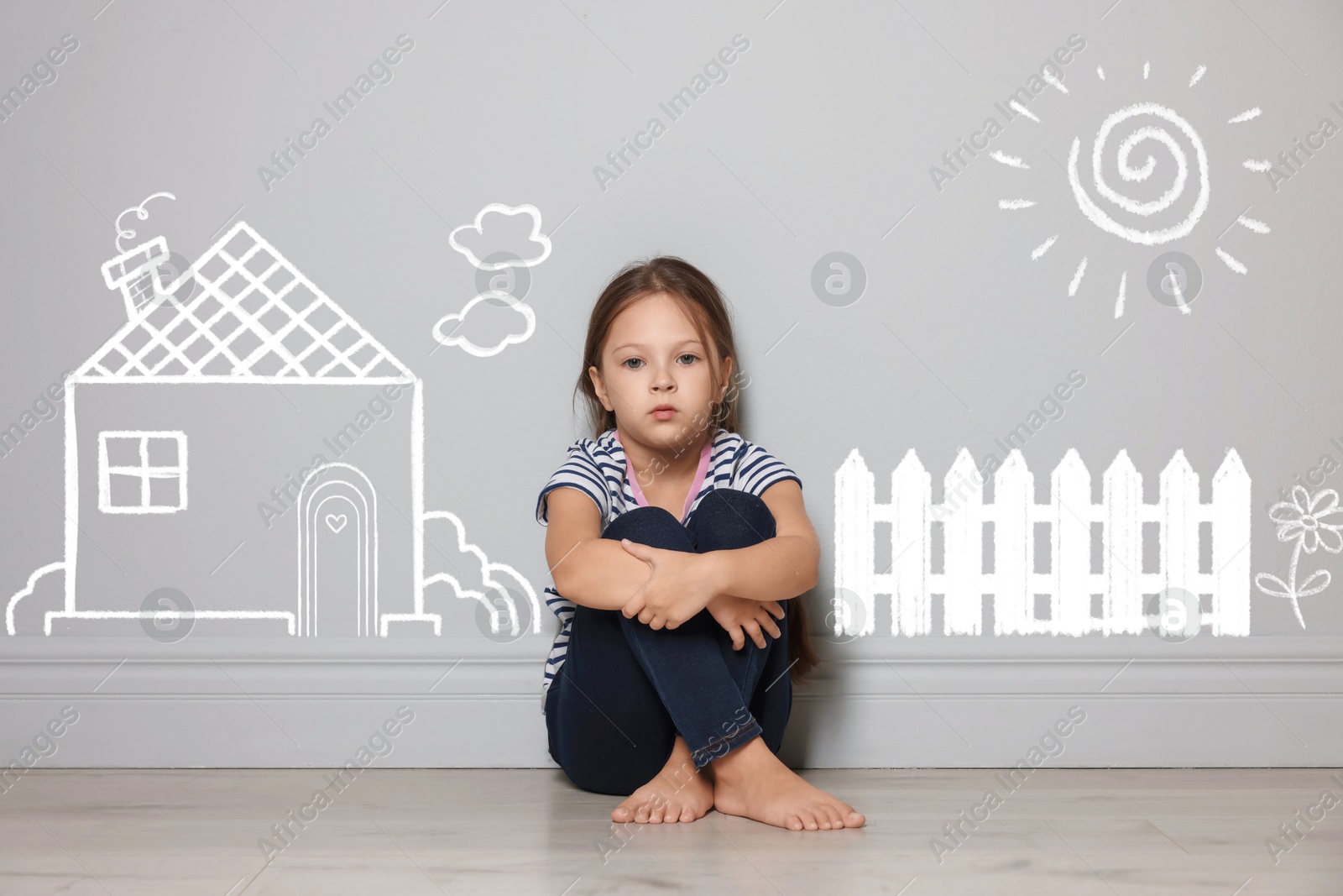 Orphanage. Sad little girl on floor near grey wall with drawings of house, fence, sun and flower Image of Orphanage. Sad little girl on floor near grey wall with drawings of house, fence, sun and flower