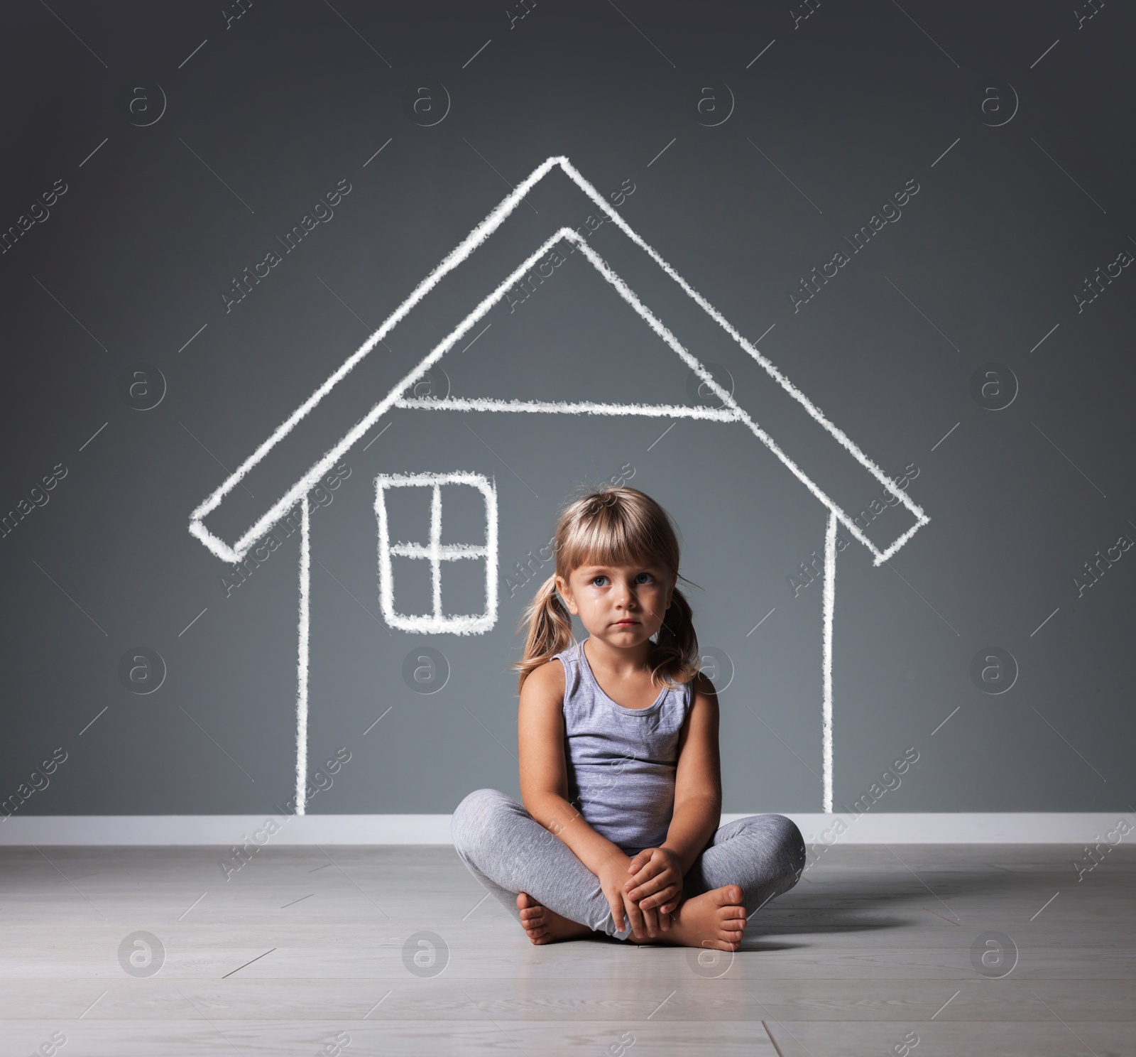 Image of Orphanage. Sad little girl on floor near grey wall with drawing of house