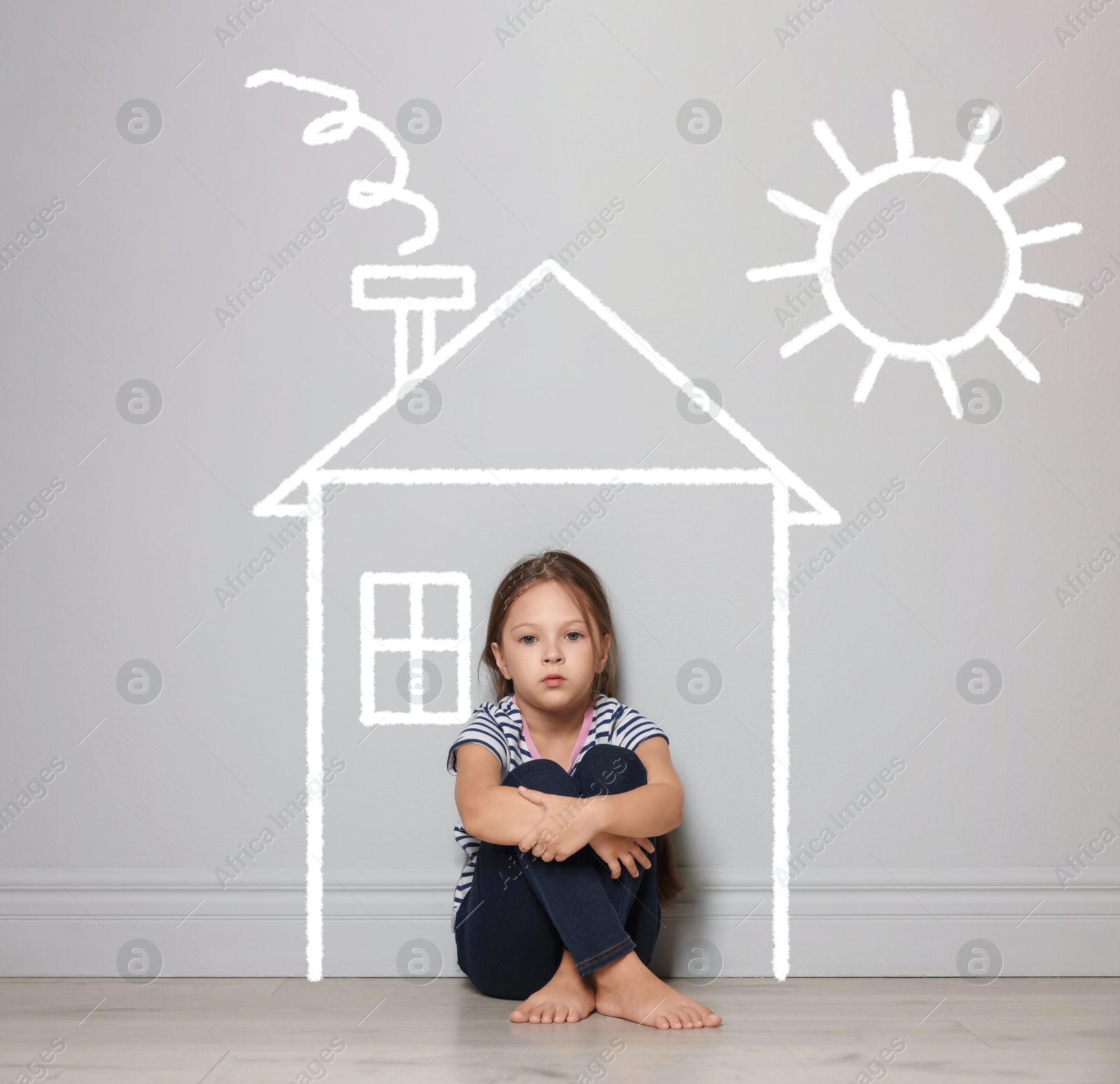Image of Orphanage. Sad little girl on floor near grey wall with drawing of house and sun