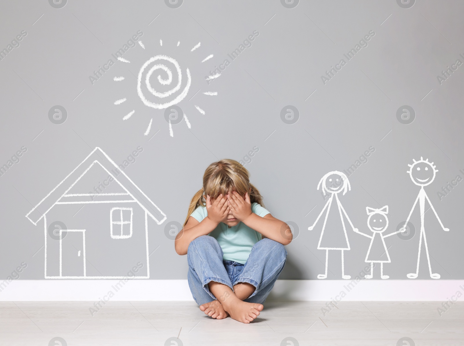 Orphanage. Sad little girl on floor near grey wall with drawings of house, family and sun Image of Orphanage. Sad little girl on floor near grey wall with drawings of house, family and sun