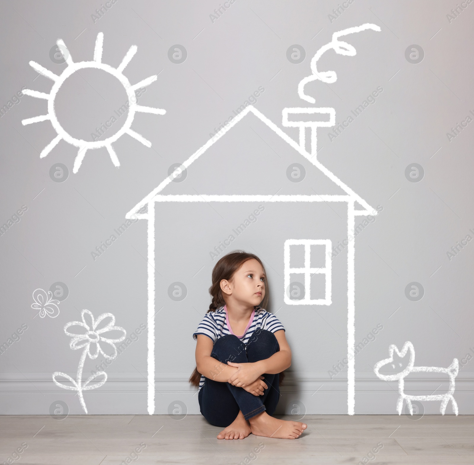 Image of Orphanage. Sad little girl on floor near grey wall with drawings of house, dog, sun and flower