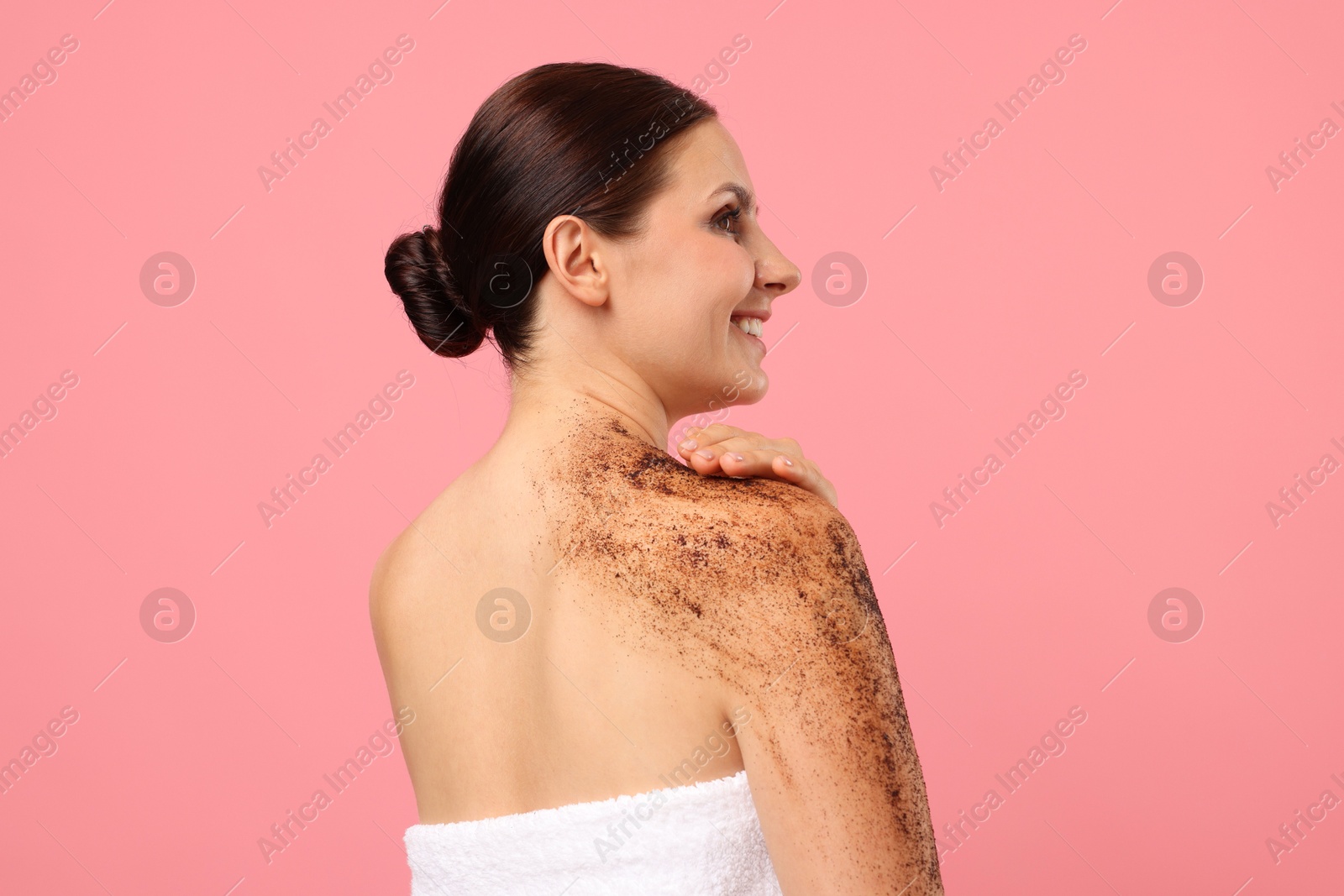 Smiling woman applying body scrub onto her shoulder against pink background Photo of Smiling woman applying body scrub onto her shoulder against pink background