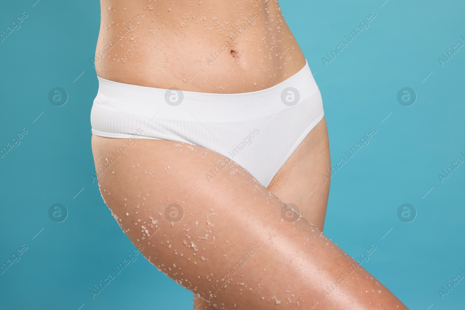 Photo of Woman with body scrub on her skin against light blue background, closeup