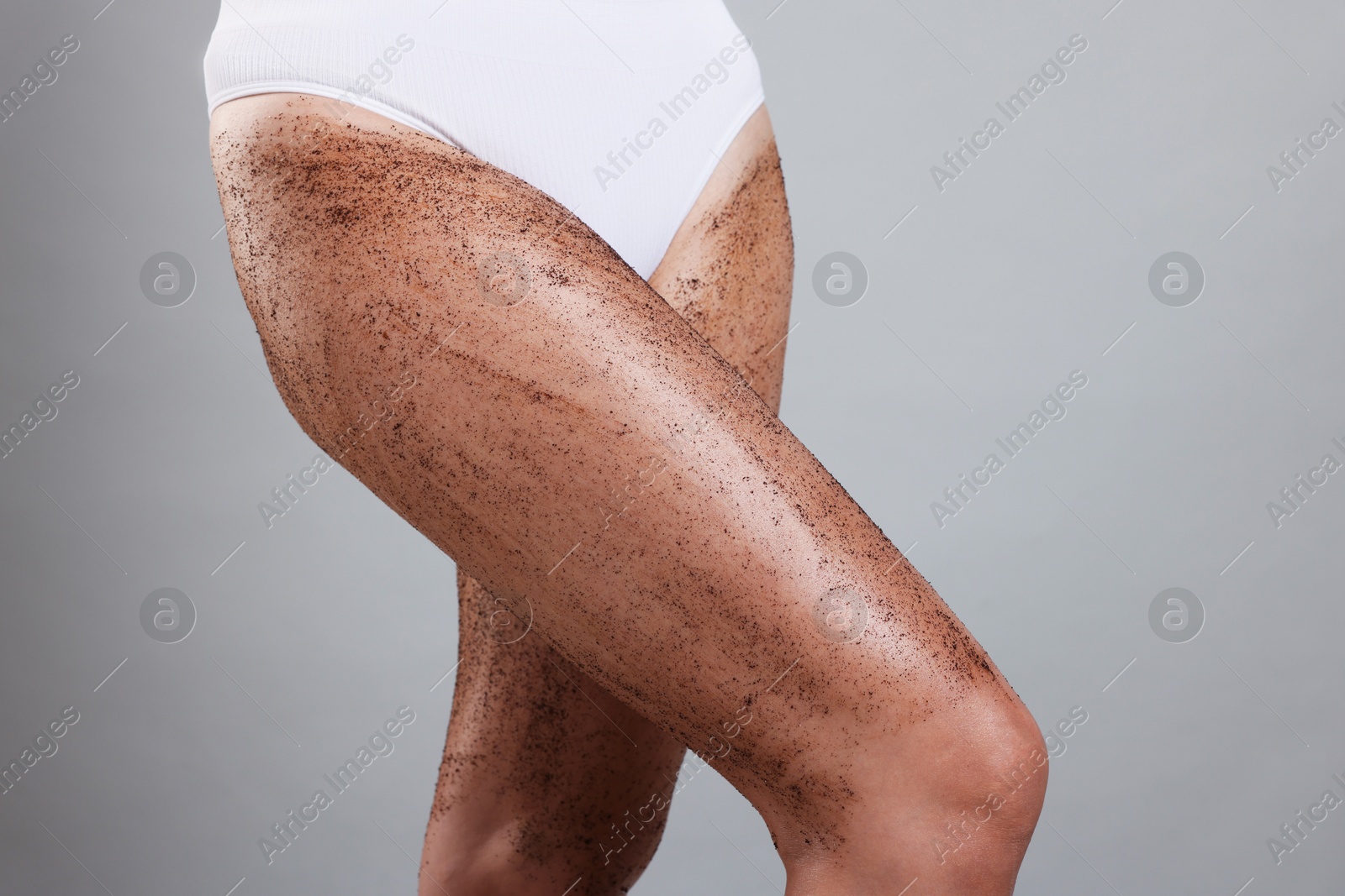 Photo of Woman with body scrub on her legs against grey background, closeup