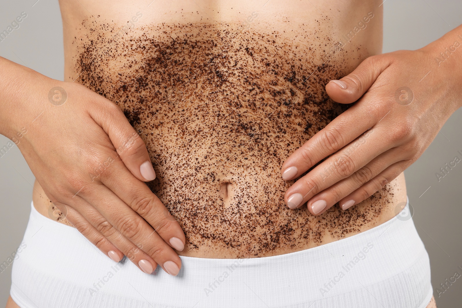 Photo of Woman applying body scrub onto her belly against grey background, closeup