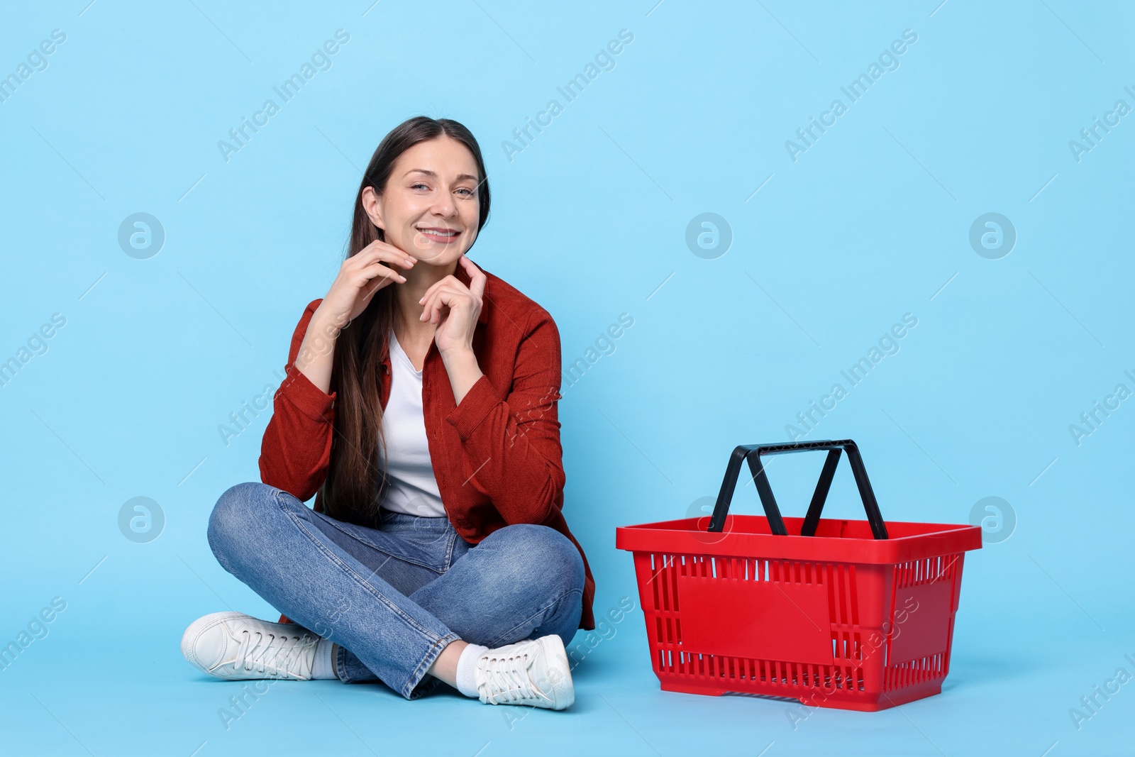 Smiling woman and shopping basket on light blue background Photo of Smiling woman and shopping basket on light blue background