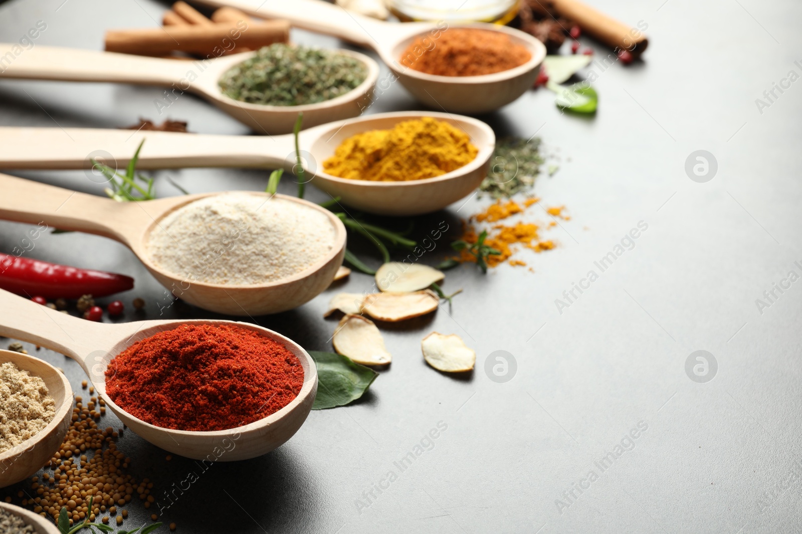 Many different spices in spoons on grey table, closeup. Space for text Photo of Many different spices in spoons on grey table, closeup. Space for text