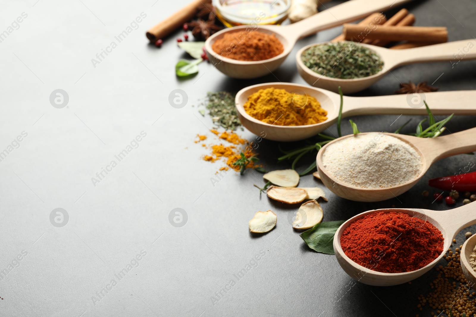 Many different spices in spoons on grey table, closeup. Space for text Photo of Many different spices in spoons on grey table, closeup. Space for text