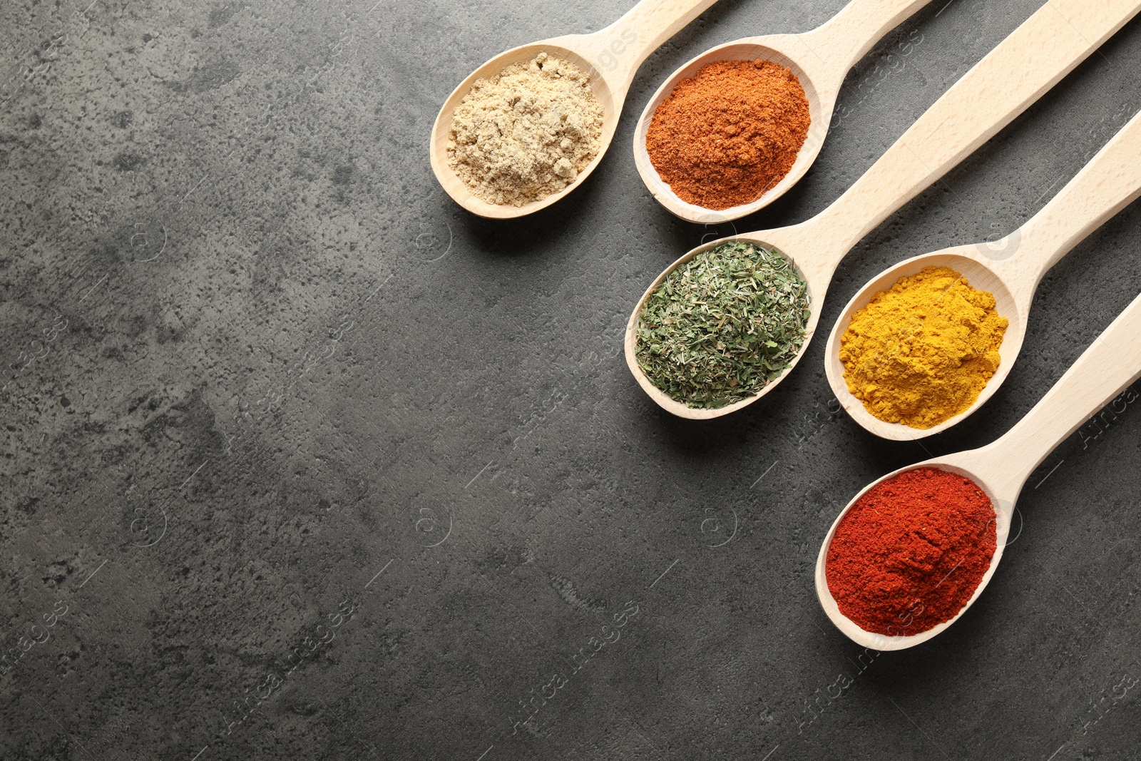 Photo of Many different spices in spoons on grey table, flat lay. Space for text