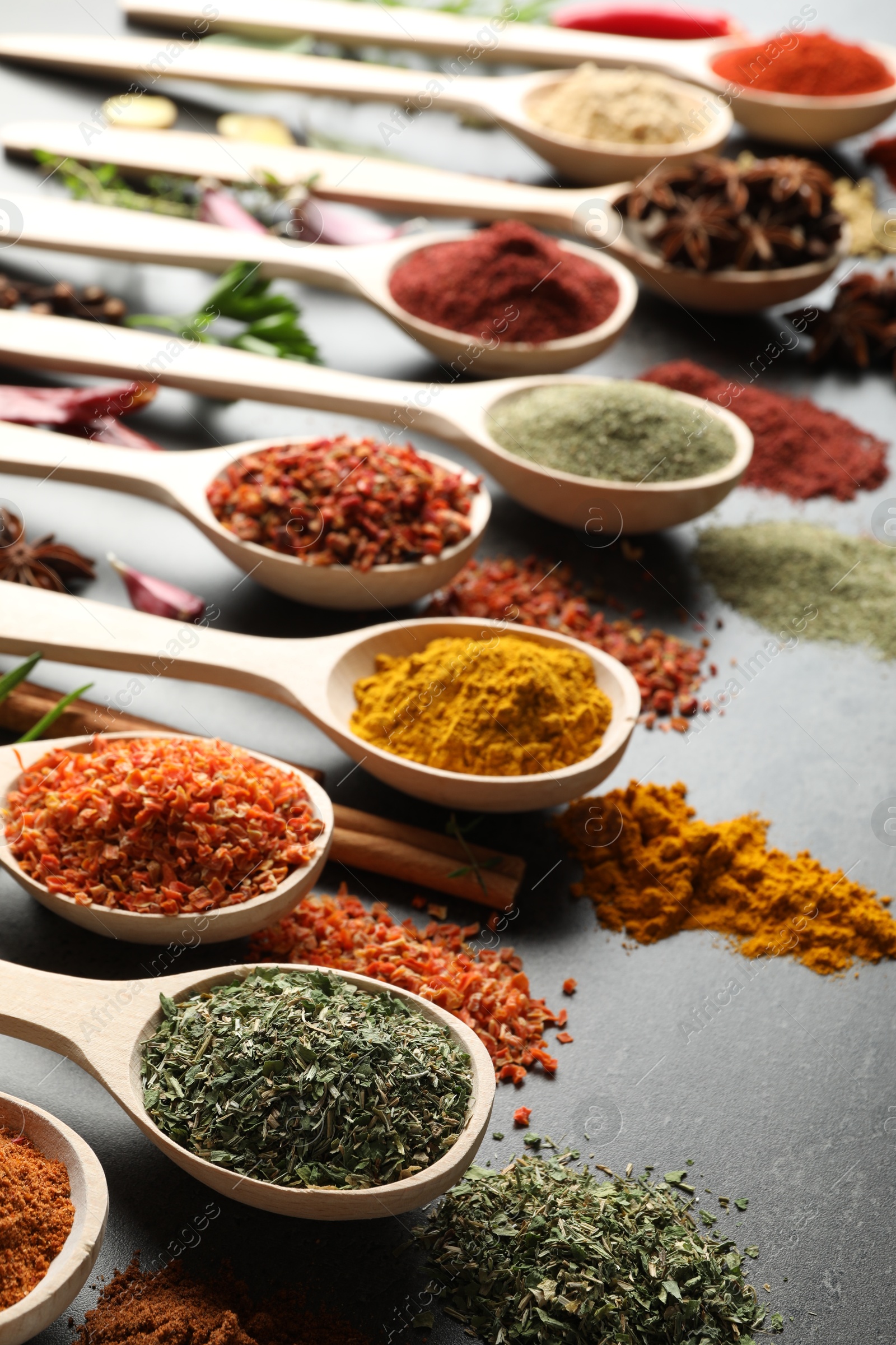 Many different spices in spoons on grey table, closeup Photo of Many different spices in spoons on grey table, closeup