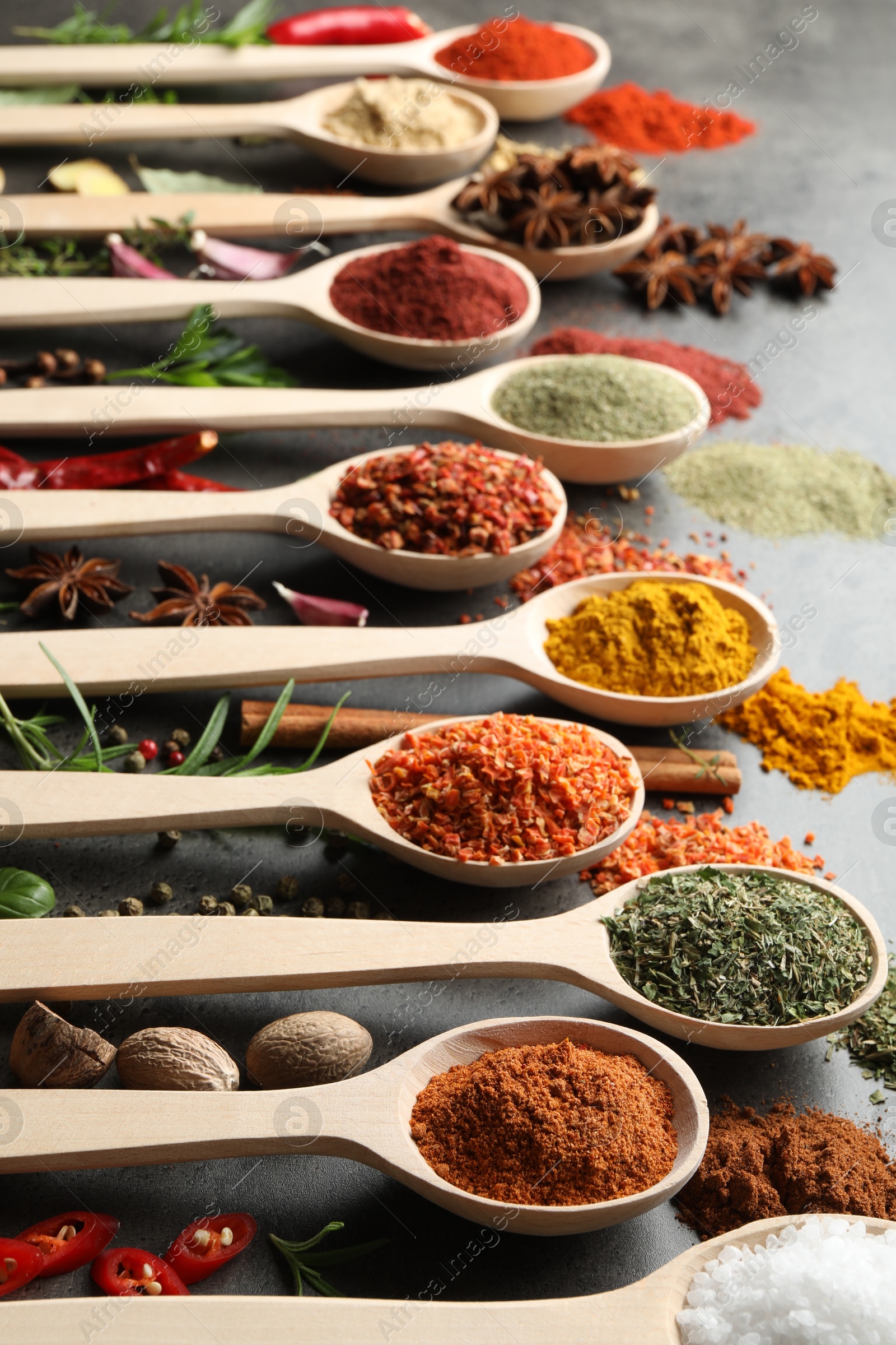 Many different spices in spoons on grey table, closeup Photo of Many different spices in spoons on grey table, closeup