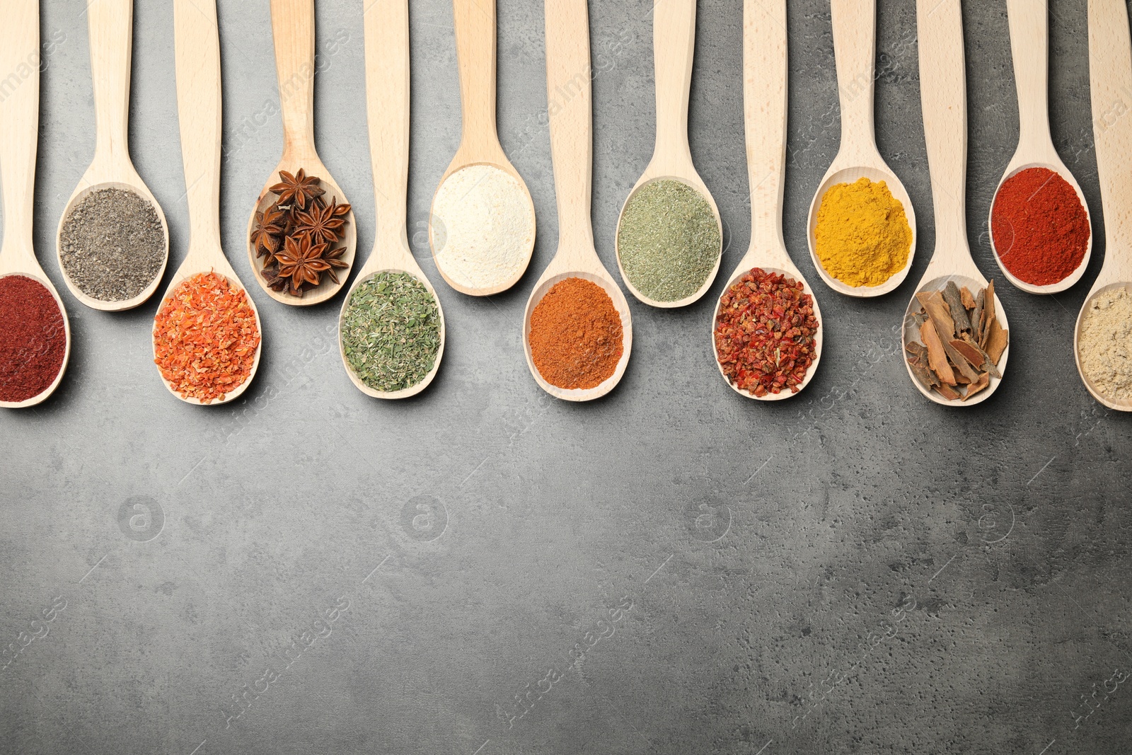 Photo of Many different spices in spoons on grey table, flat lay. Space for text