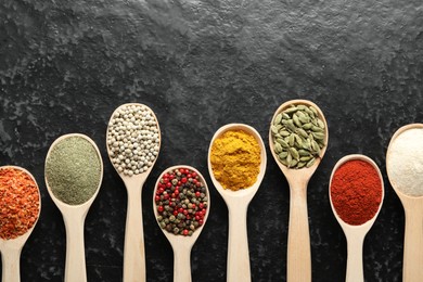 Photo of Many different spices in spoons on black table, flat lay. Space for text