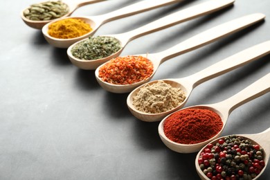 Photo of Many different spices in spoons on grey table, closeup