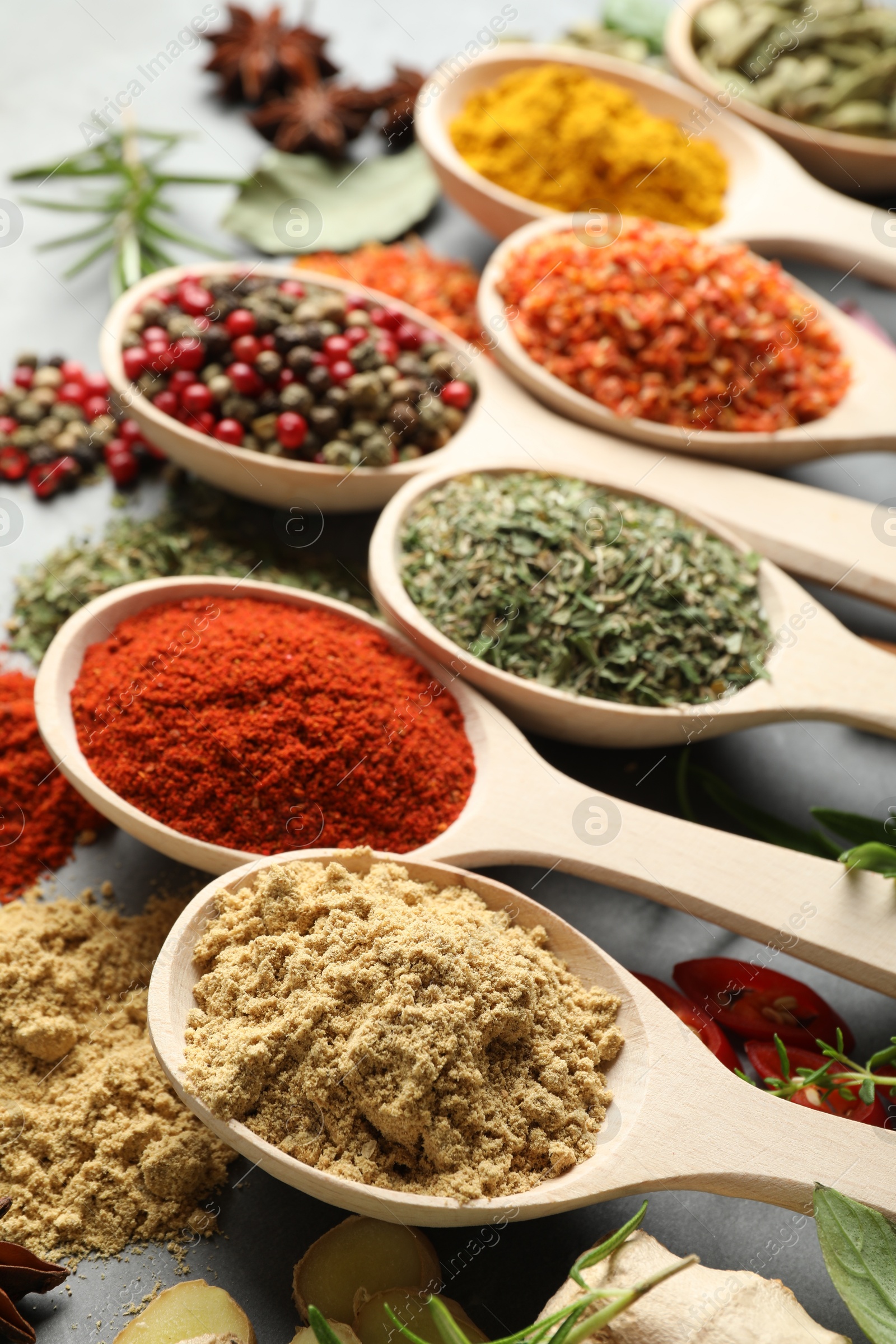 Many different spices in spoons on grey table, closeup Photo of Many different spices in spoons on grey table, closeup