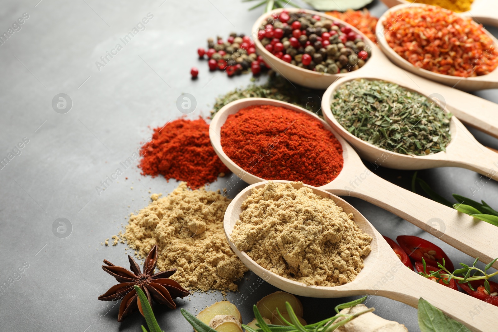 Many different spices in spoons on grey table, closeup Photo of Many different spices in spoons on grey table, closeup