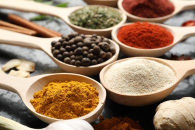 Photo of Many different spices in spoons on black table, closeup