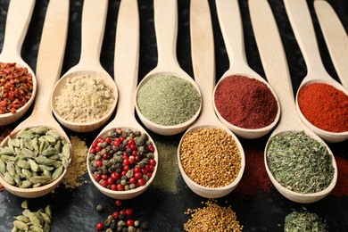 Photo of Many different spices in spoons on black table, closeup