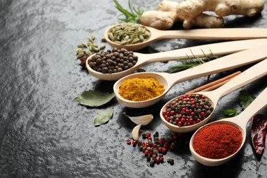 Photo of Many different spices in spoons on black table, closeup. Space for text