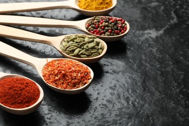 Photo of Many different spices in spoons on black table, closeup