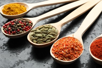 Photo of Many different spices in spoons on black table, closeup