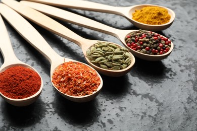Photo of Many different spices in spoons on black table, closeup