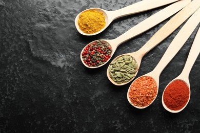 Photo of Many different spices in spoons on black table, flat lay. Space for text